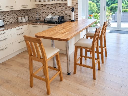Three Billy tall oak breakfast stools with cream leather seats beside an oak breakfast bar in a cream kitchen overlooking the garden