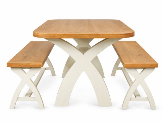 Country Oak 140cm rounded corner dining table with two matching 120cm cream painted cross leg benches viewed at an angle on a white background