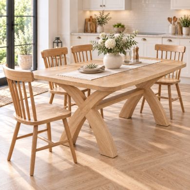 Doveridge 180cm whitewash limed oak cross-leg dining table with rounded corners and spindleback chairs in a bright kitchen.