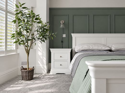 Toulouse White Painted 2 Drawer Large Assembled Bedside Table beside a matching Toulouse white bed with sage bedding and basketed tree in a green panelled bedroom