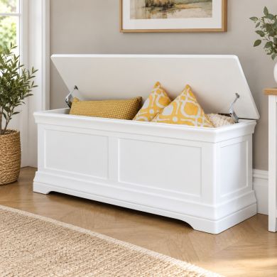 Toulouse Large White Painted Assembled Blanket Storage Box Ottoman with lid open, showing spacious interior storage with decorative cushions in a bright neutral room.