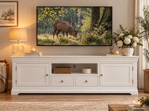 Toulouse white painted 210cm TV unit with two doors and two drawers in a cosy living room beneath a television showing woodland deer