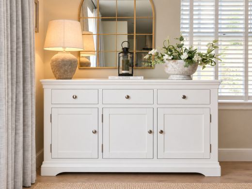 Toulouse 140cm white painted sideboard with chrome knobs, styled with a stone lamp, black lantern and white flowers beneath an arched gold-framed mirror