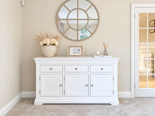 Toulouse 140cm white painted sideboard beneath a round mirror, styled with roses, framed floral artwork and a reed diffuser