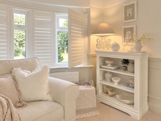 Toulouse white painted low bookcase with three open compartments beside a cream armchair in a bright living room