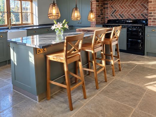 Three Java Cross solid oak bar stools beside a kitchen island beneath glowing glass pendant lights