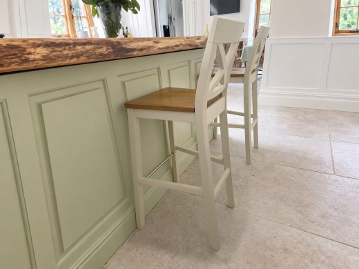 Two Java Cross cream painted bar stools with solid oak seats beside a sage green kitchen island