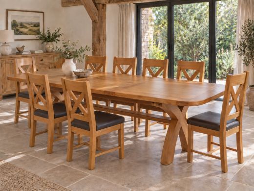 Country Oak 180–230cm cross-leg extending dining table with rounded corners and eight brown-seat oak chairs in a sunlit, oak-beamed dining room