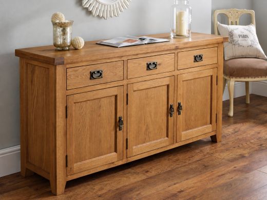Country Oak 160cm large three-door sideboard styled with a vase, open magazine and glass candle holder