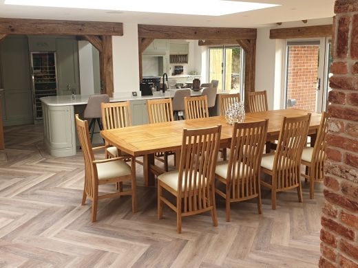 Chateaux solid oak dining table with cream-seat slatted oak chairs in a beamed kitchen with a brick column and herringbone floor